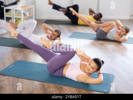 Femme asiatique effectue des exercices pour renforcer les muscles abdominaux pendant l'entraînement multinational de groupe Banque D'Images