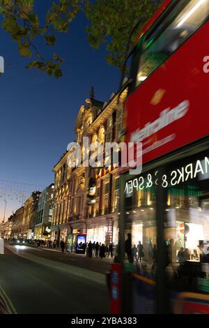 Vue nocturne d'Oxford Street, Londres. Des piétons et un bus rouge londonien passent devant les bâtiments emblématiques illuminés. Banque D'Images