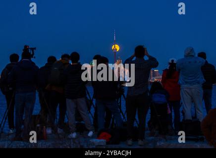 Toronto, Canada. 17 octobre 2024. Les gens filment la pleine lune se levant au-dessus de la ligne d'horizon à Toronto, Canada, le 17 octobre 2024. Crédit : Zou Zheng/Xinhua/Alamy Live News Banque D'Images