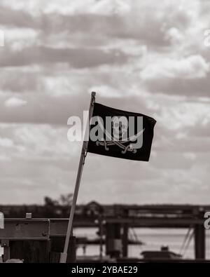 Drapeau pirate Jolly Roger soufflant dans le vent dans un cadre côtier. Banque D'Images