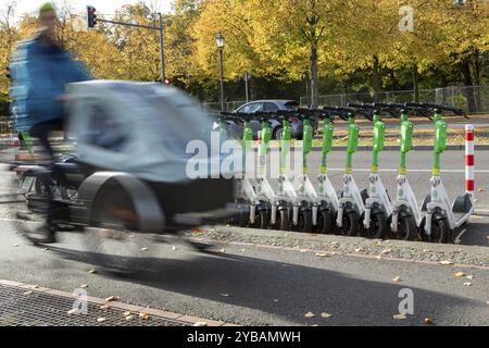 Trafic, mobilité, flou de mouvement, cycliste avec vélo cargo et e-scooters alignés du fournisseur Lime en automne dans une rue de Berlin, Allemagne, Europ Banque D'Images
