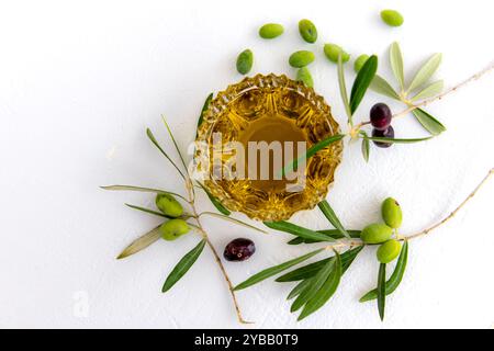 Huile d'olive dans un bol en verre cristal, olives vertes et noires en branches et olives vertes en vrac, isolées en blanc. Banque D'Images