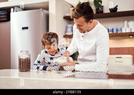 Lait, céréales et père avec enfant dans la cuisine pour le petit déjeuner à la maison le week-end pour le collage. Heureux, porridge et papa aidant garçon à préparer le matin Banque D'Images