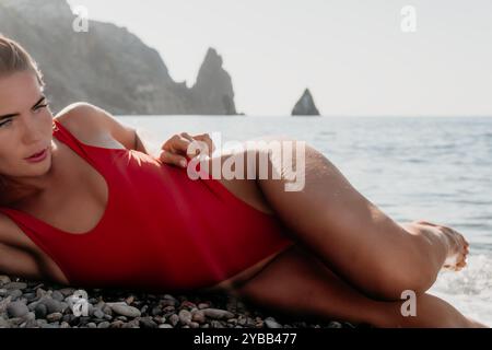 Femme en maillot de bain rouge couchée sur une plage de galets Banque D'Images