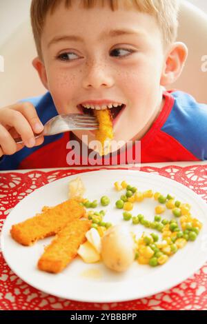 Jeune garçon mangeant les bâtonnets de poisson et légumes Banque D'Images