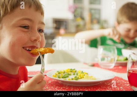 Jeune garçon mangeant les bâtonnets de poisson et légumes Banque D'Images