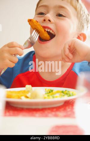 Jeune garçon mangeant les bâtonnets de poisson et légumes Banque D'Images