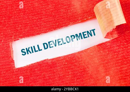 Concept commercial. La phrase, le texte, le mot DÉVELOPPEMENT DES COMPÉTENCES est écrit sur du papier blanc sous du papier déchiré rouge. Banque D'Images