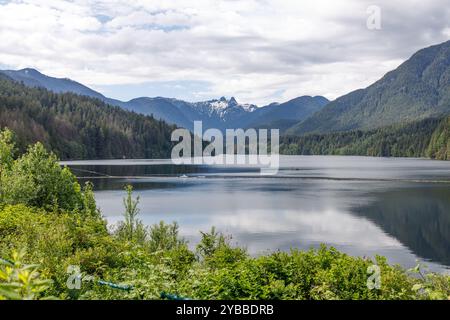 Une vue sereine sur le réservoir Capilano entouré d'une forêt dense, avec les majestueux Lions Peaks en arrière-plan Banque D'Images