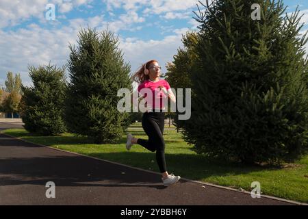 Coureuse féminine dans un parc, jogging avec des écouteurs par temps clair. Banque D'Images