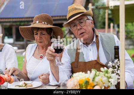 Couple mature dans des chapeaux d'été savourant du vin et repas gastronomique à une table en plein air. Les aînés élégants apprécient le style de vie de la retraite avec dîner en plein air, Banque D'Images