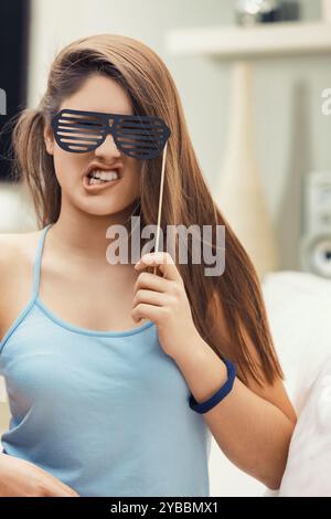 Jeune femme tient ludique de fausses lunettes, souriant largement dans un cadre décontracté et amusant, rayonnant de joie et de positivité Banque D'Images