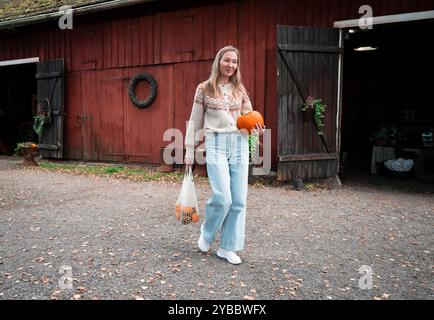 Femme tenant une grande citrouille et des citrouilles décoratives dans un sac en maille Banque D'Images