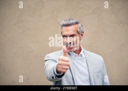 Portrait, sourire et pouces vers le haut avec homme d'affaires sur fond de mur pour la motivation, le soutien ou merci. Bonus, promotion et succès avec Happy Banque D'Images