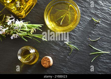 Détail de l'huile de romarin dans des récipients en verre avec des brindilles fraîches sur la table en ardoise. Vue de dessus. Banque D'Images