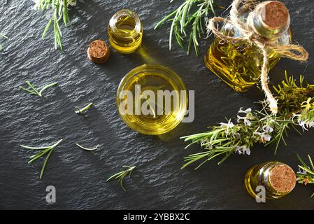 Huile essentielle de romarin dans des récipients en verre avec des brindilles fraîches sur une base d'ardoise. Vue de dessus. Banque D'Images