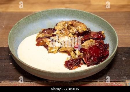 Une assiette de délicieux crumble de prunes et de mûres sur une table de cuisine en bois ou un plan de travail Banque D'Images