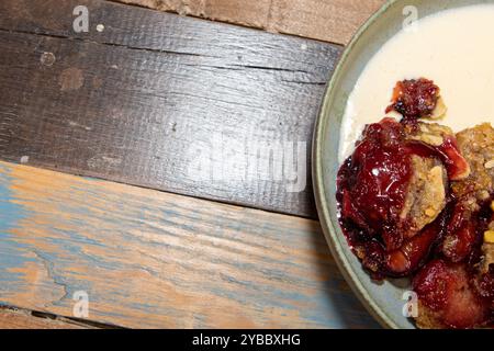 Une assiette de délicieux crumble de prunes et de mûres sur une table de cuisine en bois ou un plan de travail Banque D'Images