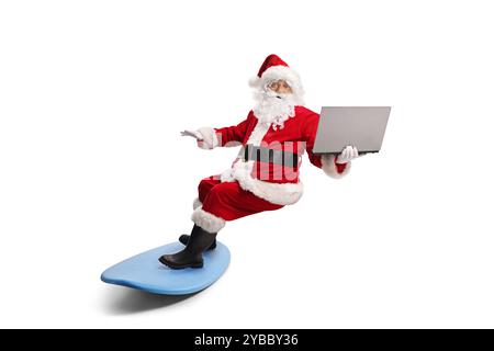 Père noël chevauchant une planche de surf et tenant un ordinateur portable isolé sur fond blanc Banque D'Images