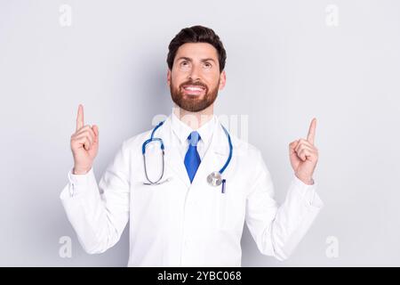 Portrait de l'homme de docteur expérimenté regarder indiquent les doigts vers le haut de l'espace vide porter manteau blanc isolé sur fond de couleur grise Banque D'Images