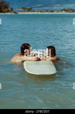 Couple reposant sur une planche de surf souriant Banque D'Images