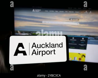 Personne tenant un smartphone avec le logo de la société Auckland International Airport Limited sur l'écran en face du site Web. Concentrez-vous sur l'affichage du téléphone. Banque D'Images