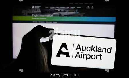 Personne tenant le téléphone portable avec le logo de la société Auckland International Airport Limited sur l'écran en face de la page Web. Concentrez-vous sur l'affichage du téléphone. Banque D'Images