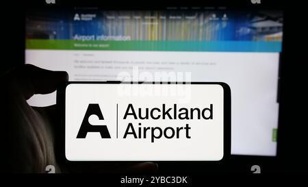 Personne tenant le téléphone portable avec le logo de la société Auckland International Airport Limited sur l'écran en face de la page Web. Concentrez-vous sur l'affichage du téléphone. Banque D'Images