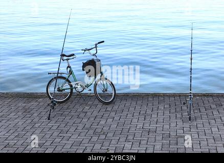 Temps de pêche : deux tiges et un vieux vélo vert sur la jetée en béton près du lac Banque D'Images