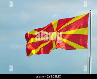 Drapeau macédonien agitant dans le vent : couleurs nationales rouge et jaune contre un ciel bleu clair Banque D'Images