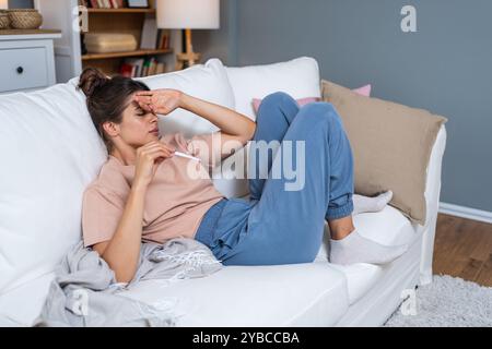 Concept de problème de virus saisonnier de maladie. Femme malade ayant la grippe couchée sur le canapé tenant le thermomètre. Femelle malade couchée dans le lit avec une forte fièvre. Froid Banque D'Images
