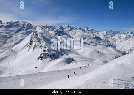 Skieurs et snowboarders descendant les pistes dans la station de ski des Menuires. Activités de sports d'hiver surplombant les montagnes enneigées dans les trois vallées. Banque D'Images