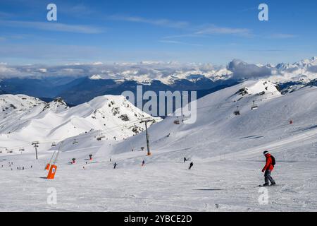 Skieurs et snowboarders descendant les pistes dans la station de ski des Menuires. Activités de sports d'hiver surplombant les montagnes enneigées dans les trois vallées. Banque D'Images