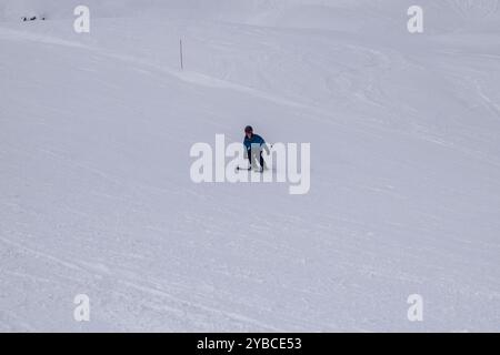 Jeune skieur masculin en action ski alpin dans une station de ski européenne. Vue latérale du skieur descendant dans la station d'hiver les Menuires, France. Banque D'Images