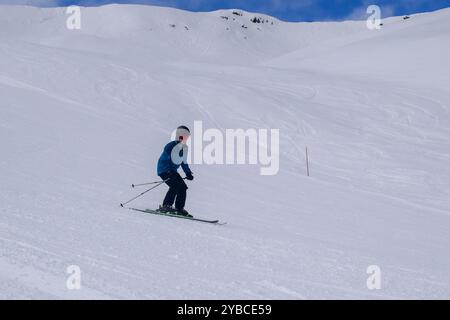 Jeune skieur masculin en action ski alpin dans une station de ski européenne. Vue latérale du skieur descendant dans la station d'hiver les Menuires, France. Banque D'Images