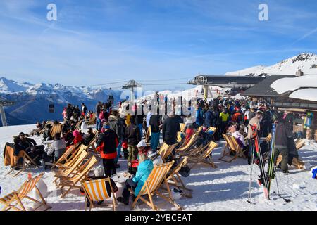 Les Menuires - 13 mars 2024 : Apres ski party par une piste de ski active dans la station de ski française les Menuires. Skieurs buvant à côté des montagnes enneigées. Banque D'Images