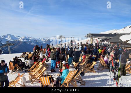 Les Menuires - 13 mars 2024 : Apres ski party par une piste de ski active dans la station de ski française les Menuires. Skieurs buvant à côté des montagnes enneigées. Banque D'Images