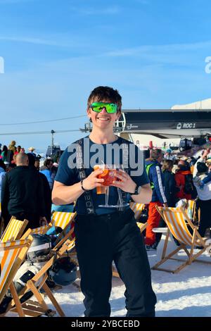 Les Menuires, France - 13 mars 2024 : jeune skieur masculin avec boissons et cocktails à un événement après ski dans la station de ski des Menuires dans les trois Vallées Banque D'Images