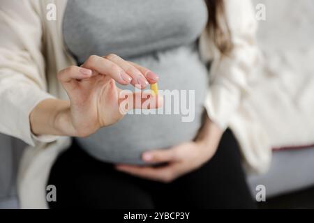 Gros plan de jeune femme enceinte tenant la pilule à la main, prenant des vitamines d, E, A, calcium, compléments alimentaires à la maison. Grossesse, santé prénatale et w Banque D'Images