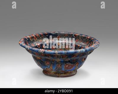 Bol en mosaïque, fin du 1er siècle av. J.-C.-1er siècle A.D. informations supplémentaires : bol en verre moulé en mosaïque composé par affaissement d'une série de cannes sectionnelles de bleu foncé (cobalt) combinées avec deux autres types de cannes (l'une d'un centre jaune cerné de rouge et noir avec un point blanc au centre, et un autre type avec un point blanc au centre du rouge et cerné de noir avec des points blancs) pour créer un motif de fleur décoratif. Le pied a été fait en chauffant une longueur de la chaîne de fleurs et en la tirant en cercle autour de la face inférieure du bol. Banque D'Images