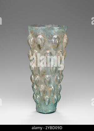 Lotus Bud Beaker, 1st Century A.D. informations supplémentaires : bécher évasé de verre verdâtre soufflé dans un moule en quatre parties (y compris la base). Six rangées de motifs gradués en forme de goutte, disposés dans des registres horizontaux décalés, décorent l'extérieur. La jante est lisse et coupée. La bouche est rehaussée par deux lignes incisées par une roue juste en dessous du bord, et un anneau concentrique articule le fond du récipient au-dessus du vase aplati. Il y a aussi deux anneaux concentriques moulés sur le fond du vase. Banque D'Images