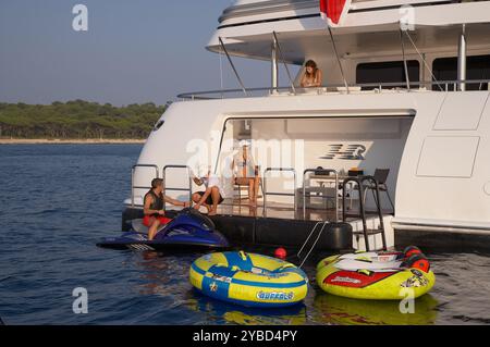 Louez les clients en vacances en profitant de la plate-forme de natation sur un superyacht avec les jouets aquatiques au premier plan. Banque D'Images