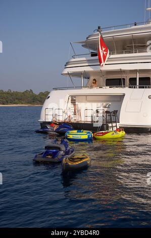 Louez les clients en vacances en profitant de la plate-forme de natation sur un superyacht avec les jouets aquatiques au premier plan. Banque D'Images