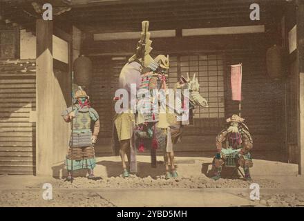 Trois guerriers japonais, 1868-1880. Portrait de trois samouraïs en armure pleine posant devant une maison. Le guerrier à gauche tient une grande lance ou bâton, le guerrier au centre est assis à cheval de profil, et le guerrier à droite est assis sur un petit tabouret. Le cheval est également vêtu d'armures. Banque D'Images