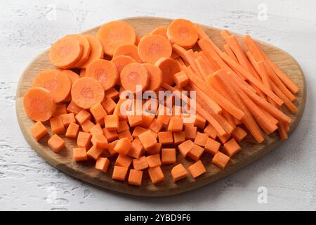 Cubes, barres, tranches de carottes fraîches mûres sur une planche de bois, trois types de légumes coupants. Alimentation saine Banque D'Images
