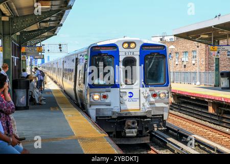 Queens, New Yok, États-Unis - 20 août 2024 : un train s'arrête dans une gare animée, avec des passagers qui attendent et profitent de la journée ensoleillée. Banque D'Images