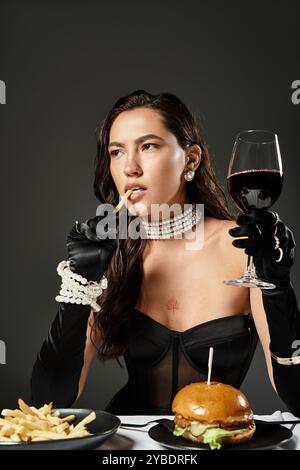 Une femme élégante savoure un verre de vin tout en dégustant des spécialités gastronomiques de fast-food. Banque D'Images