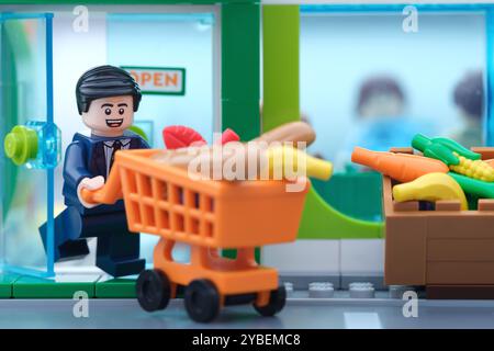 Tambov, Fédération de Russie - 18 octobre 2024 Une figurine d'homme d'affaires Lego poussant un panier plein de produits d'épicerie hors d'un supermarché. Banque D'Images