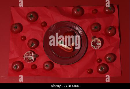 Composition de pose plate avec poivre, tomates et assiettes sur fond rouge Banque D'Images