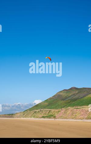 Un parapente volant dans le ciel bleu au-dessus de Rhossili Bay sur la péninsule de Gower, au sud du pays de Galles Banque D'Images